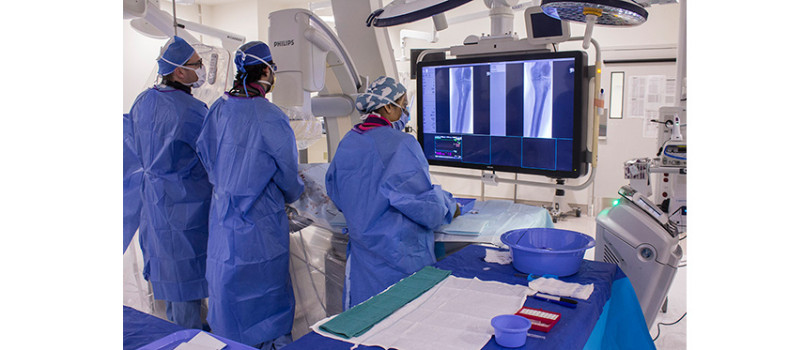 The Angiodroid is positioned at the foot of the operating table (near the bottom right, flashing a green light). By injecting carbon dioxide into the patient’s vascular system, it enables the surgical team to view blood vessels on a large screen. Among the members of the team are (from left) Vascular Surgeon Dr. Elie Girsowicz, Resident Dr. Ahmad Muqaddam and Nurse Aswathy Maria George. (Click on this or any photo to enlarge it.)