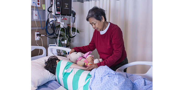 In the Palliative Care Unit at the JGH, Lucila Valerio (standing) helps her sister, Rosemarie Felipe, snuggle with a teddy bear supplied by donor Elayne Kazenel Weigensberg and her family.